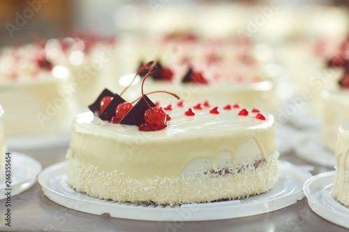 Red cherry on white cake on a table with cakes