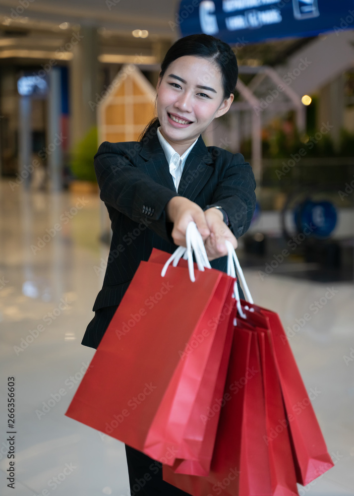 Business, people, shopping concept-Beautiful and cheerful Asian woman stands while holding shopping bag, smiles in the shopping mall. Asian woman shopping for clothes in outlet mall