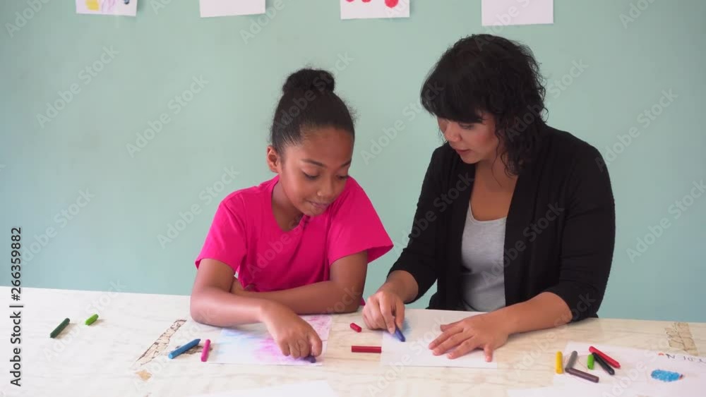 Young teacher giving African American kid an art lesson and teaching how to draw inside indoors room in natural ambient light Young teacher giving African American kid an art lesson and teaching how to draw inside indoors room in natural ambient light