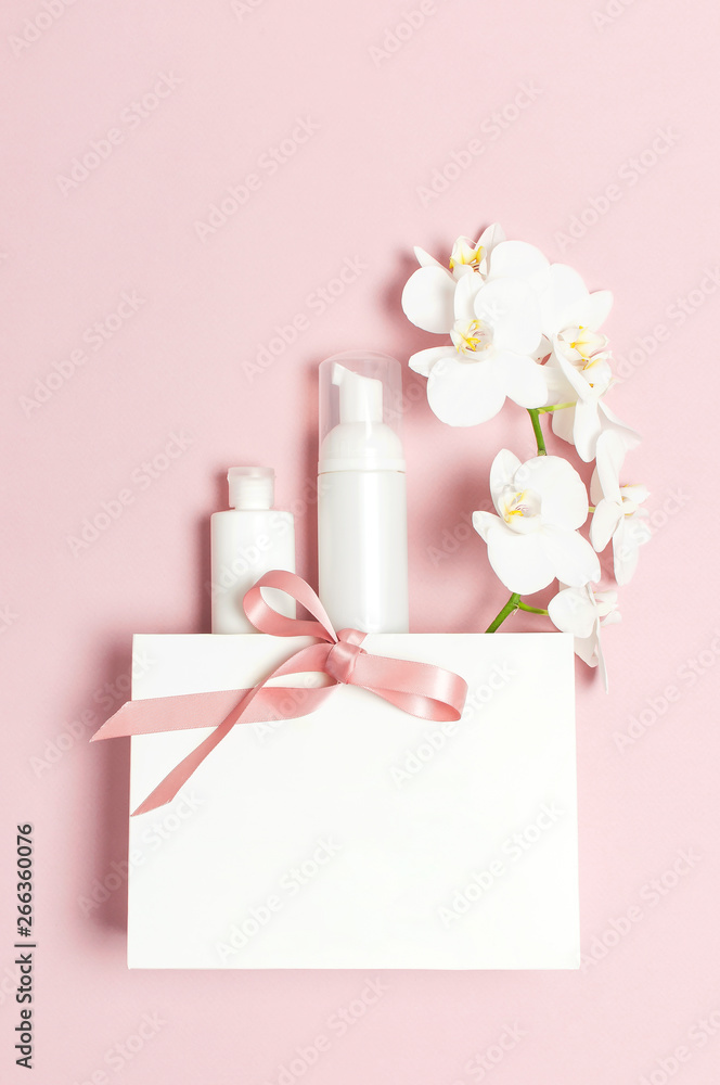 Cosmetics SPA branding mock-up. Flat lay top view White cosmetic bottle containers gift bag White Phalaenopsis orchid flowers on pink background. Natural organic beauty product concept Cosmetics SPA branding mock-up. Flat lay top view White cosmetic bottle containers gift bag White Phalaenopsis orchid flowers on pink background. Natural organic beauty product concept