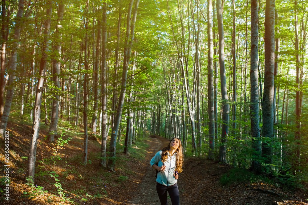 Φωτογραφία Young woman taking a walk in the forest, carrying a backpack in the forest on sunset light in the autumn season