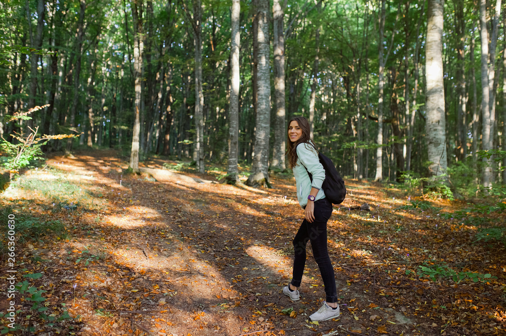 Young woman taking a walk in the forest, carrying a backpack in the forest on sunset light in the autumn season.