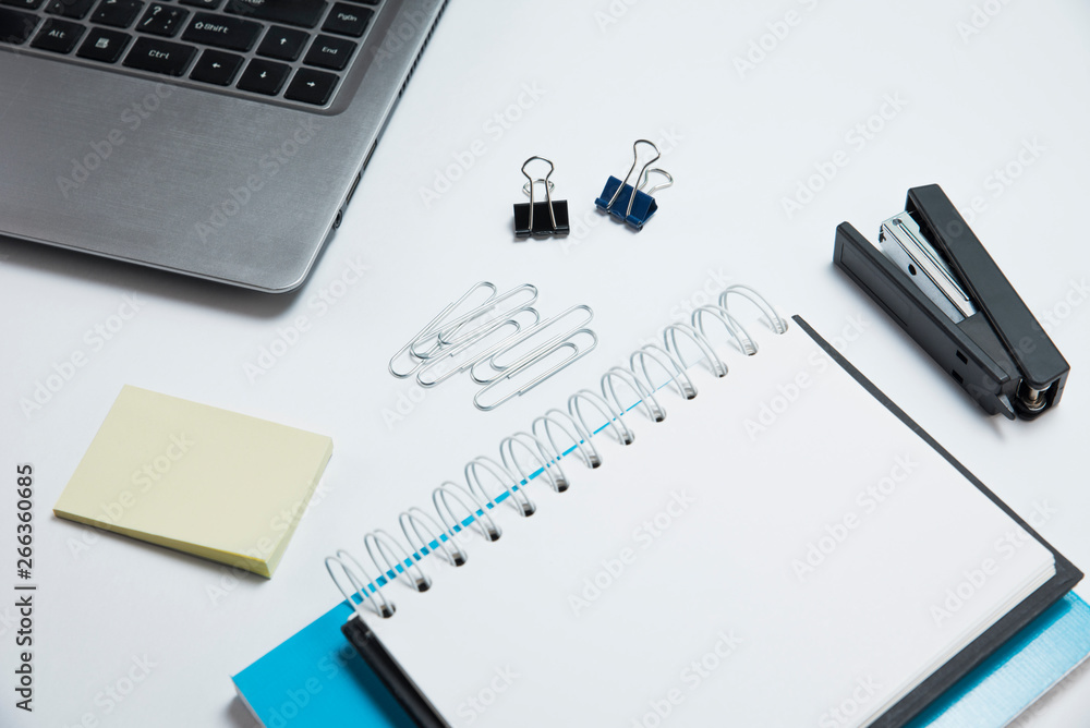 White office desk with laptop, notepad and sticker. Stationery on white background White office desk with laptop, notepad and sticker. Stationery on white background