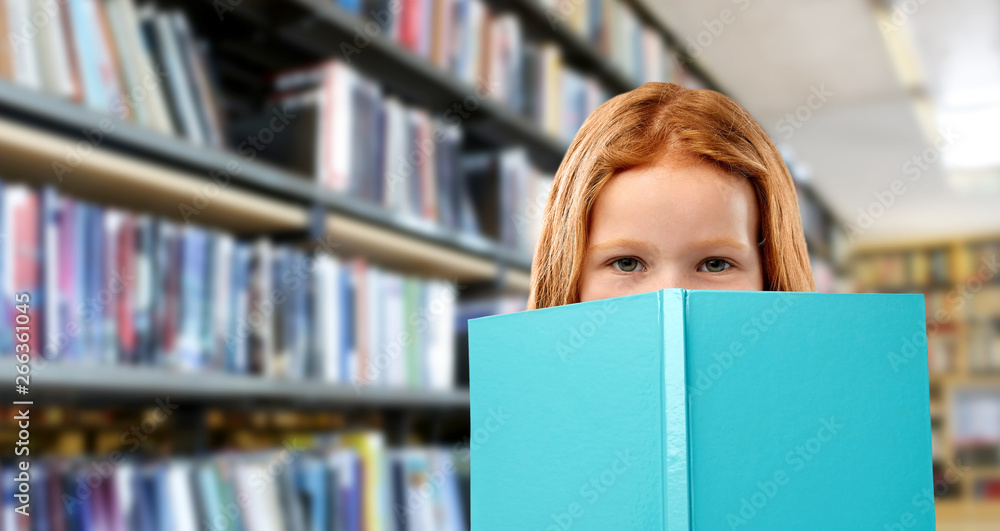 childhood and people concept - smiling red haired girl reading book over library background childhood and people concept - smiling red haired girl reading book over library background