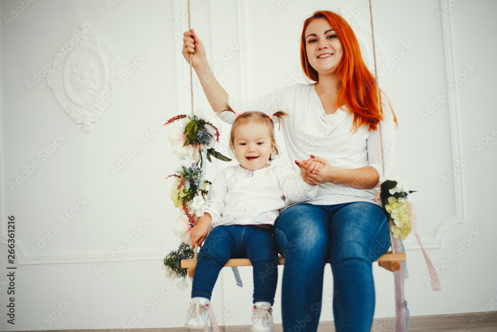 Beatuful ginger mother playing with daughter. Little girl sitting on a swing at home. Beatuful ginger mother playing with daughter. Little girl sitting on a swing at home.