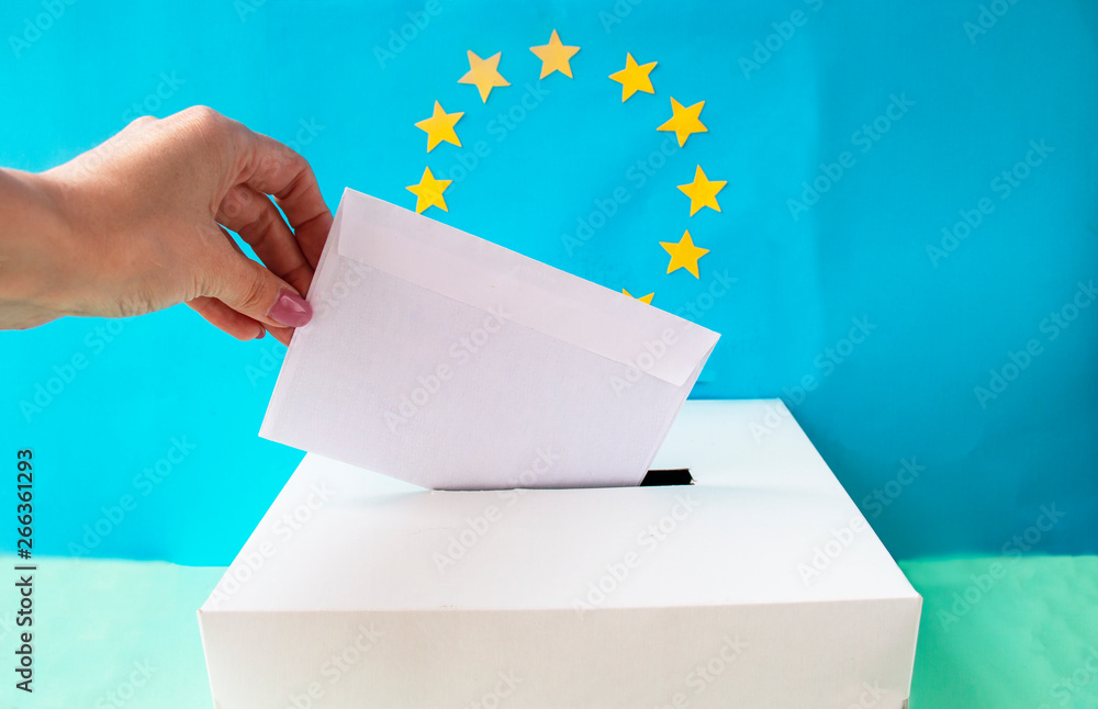 Voting slip being placed by a hand into a ballot box with the European Union flag in the background Voting slip being placed by a hand into a ballot box with the European Union flag in the background