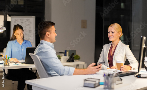 business, deadline and technology concept - businesswoman and businessman talking and drinking coffee late at night office
