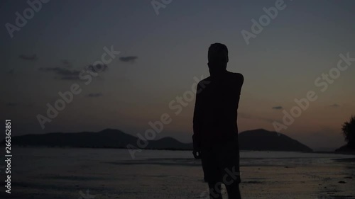 Young handsome man silhouette on the tropical beach sunset 4k.  Athletic male raises head and touches hair slow motion. Horizon with mountains and ocean on the back.