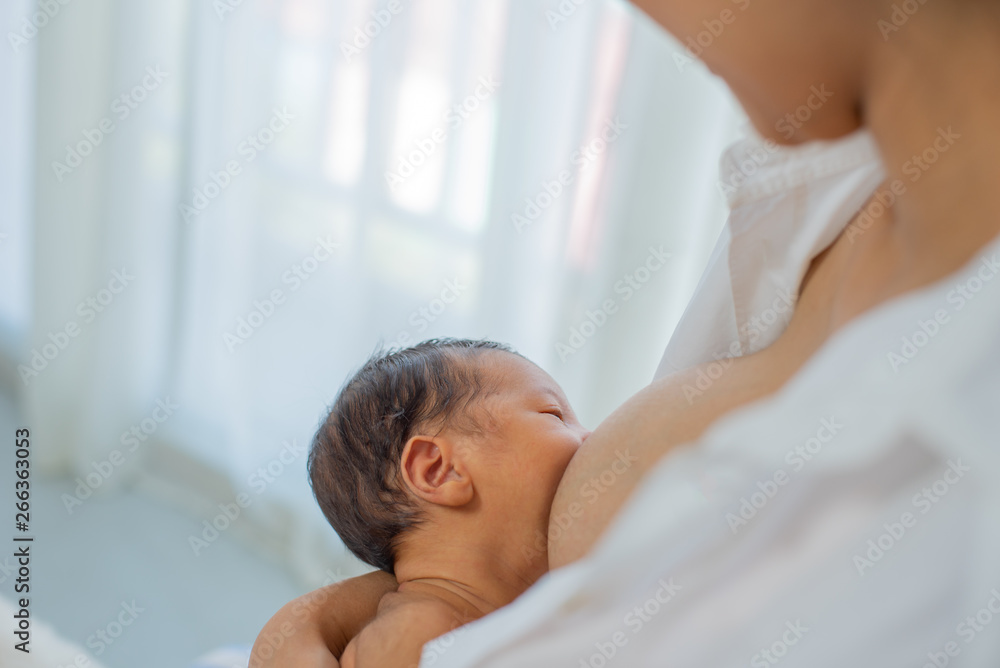 Close up view of mother give breastfeeding to little newborn with white shirt and sitting on bed white background of glass windows and curtain Close up view of mother give breastfeeding to little newborn with white shirt and sitting on bed white background of glass windows and curtain