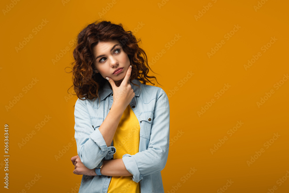 pensive redhead woman thinking while standing on orange pensive redhead woman thinking while standing on orange