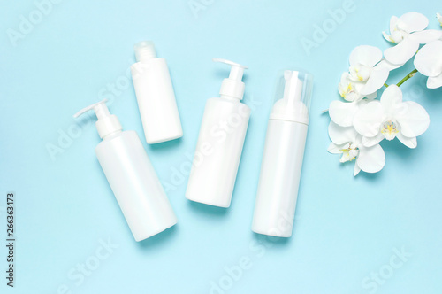 Flat lay top view White cosmetic bottle containers White Phalaenopsis orchid flowers on pastel blue background. Cosmetics SPA branding mock-up Natural organic beauty product concept Minimalism style