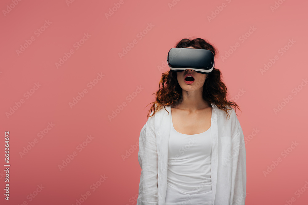 surprised curly young woman wearing virtual reality headset on pink surprised curly young woman wearing virtual reality headset on pink