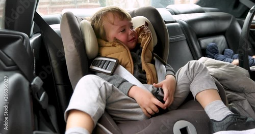 Closeup crying boy with worried stressed expression in child safety seat in car interior