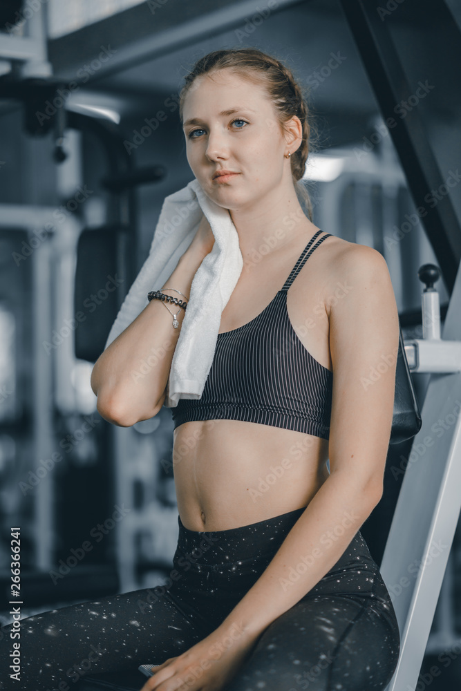 Young attractive woman caucasian sitting and using towel to wipe the sweat. Relaxation after hard workout in gym. Fitness concept, Healthy, Sport, Lifestyle Young attractive woman caucasian sitting and using towel to wipe the sweat. Relaxation after hard workout in gym. Fitness concept, Healthy, Sport, Lifestyle