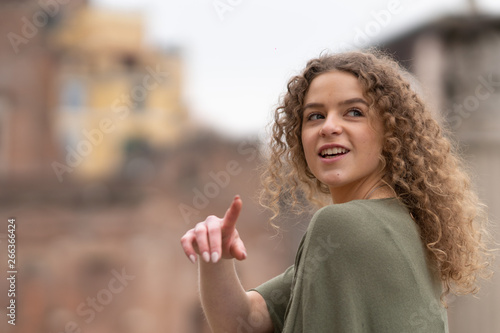 Young woman as tourist in Rome, Italy, looking and pointing at touristic site