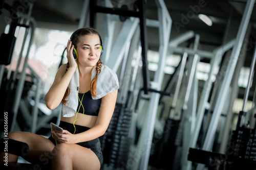 Young attractive woman caucasian sitting and listening to music by earphones connect to smart phone. Relaxation after hard workout in gym. Fitness concept, Healthy, Sport, Lifestyle