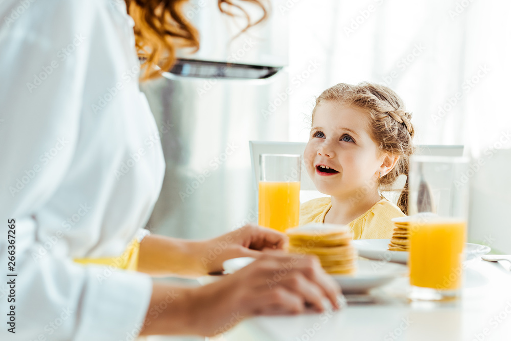 selective focus of emotional daughter looking at mother while having breakfast selective focus of emotional daughter looking at mother while having breakfast