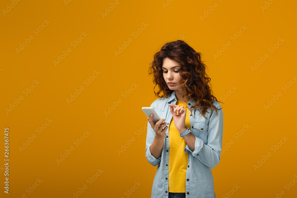 attractive curly redhead woman looking at smartphone on orange attractive curly redhead woman looking at smartphone on orange