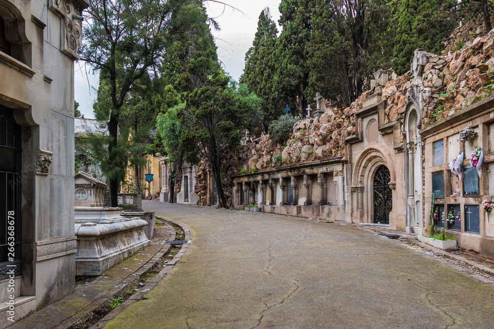 Perspective view of the curved footpath with graves and crypts on the Montjuic Cemetery in overcast day, Barcelona, Catalonia, Spain