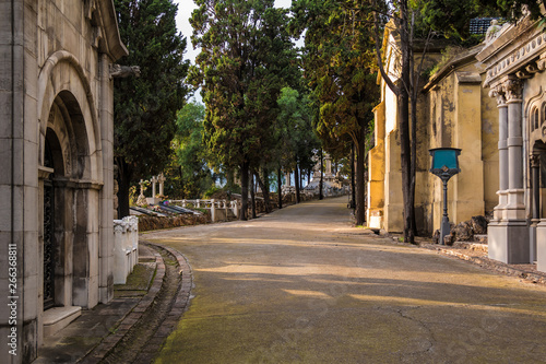 Perspective view of the curved footpath with graves and crypts on the Montjuic Cemetery in sunny day, Barcelona, Catalonia, Spain