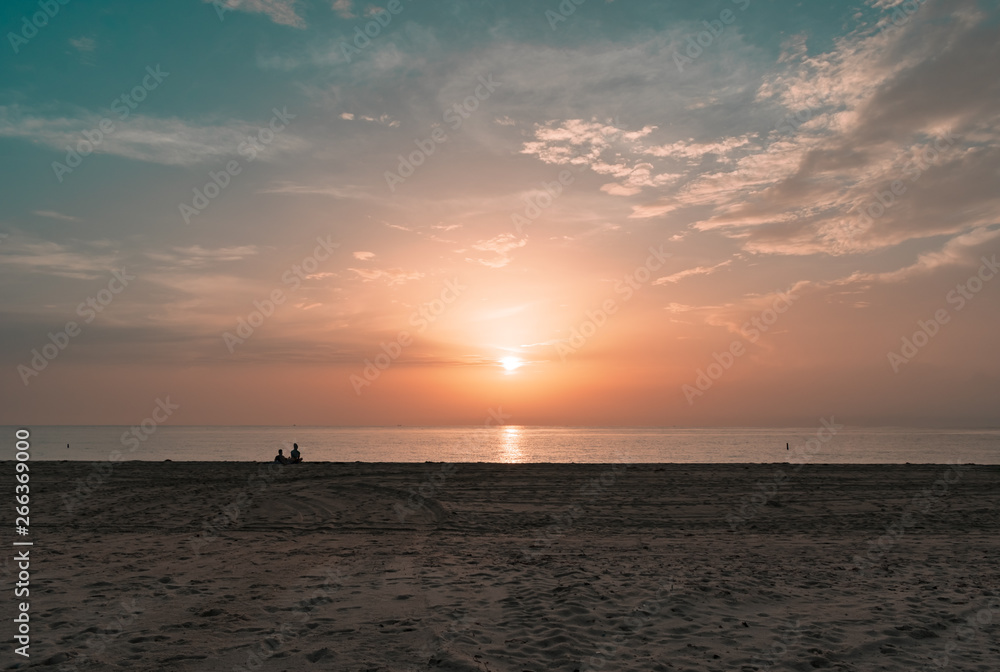 silhouette of a couple sitting on the sand watching the sun rise on a calm morning silhouette of a couple sitting on the sand watching the sun rise on a calm morning