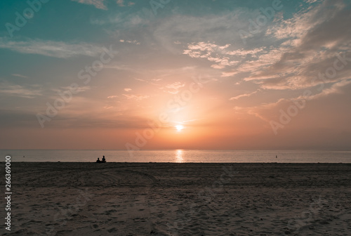 silhouette of a couple sitting on the sand watching the sun rise on a calm morning