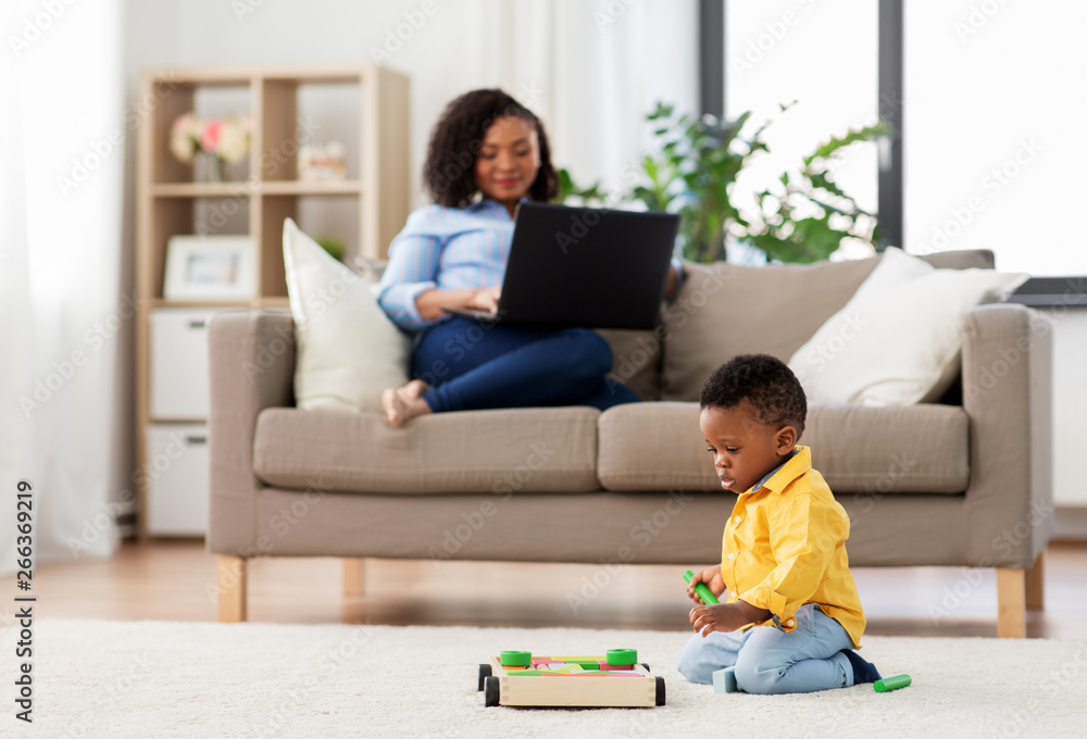 family, motherhood and people concept - african american baby playing with toy blocks kit and his mother using laptop computer at home family, motherhood and people concept - african american baby playing with toy blocks kit and his mother using laptop computer at home