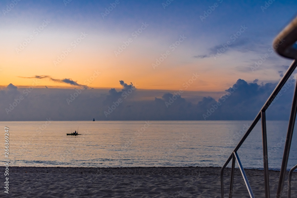 railing on the beach with small boats on the ocean at dawn