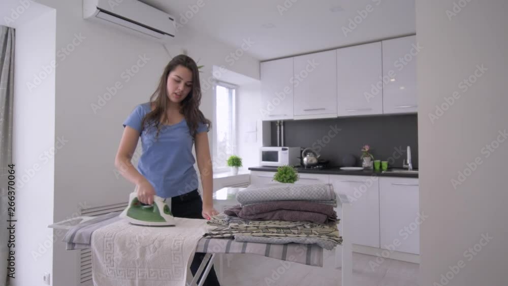 Home routines, cheerful housewife girl is ironing fresh towels and having fun and singing in room