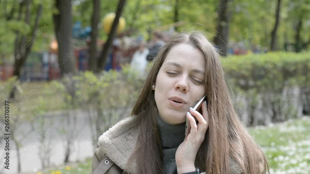 Woman smiling and talking on mobile phone in city park Woman smiling and talking on mobile phone in city park