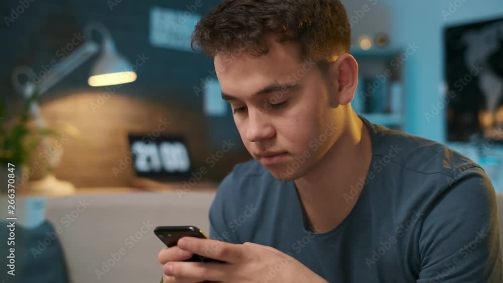 Close-up portrait of a young boy typing a message on his phone with the lighs on in the evening Close-up portrait of a young boy typing a message on his phone with the lighs on in the evening