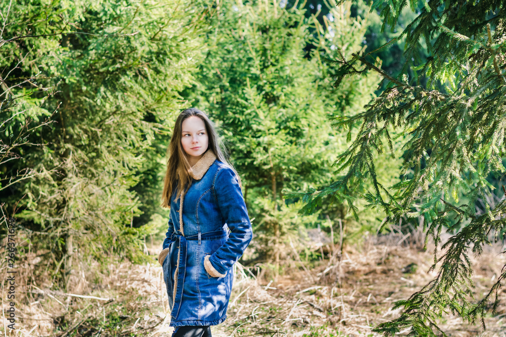 Beautiful young girl with long blond hair in a blue denim jacket in a green forest on a sunny spring day Beautiful young girl with long blond hair in a blue denim jacket in a green forest on a sunny spring day