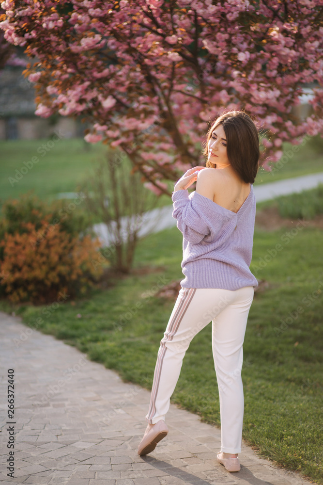 Attractive young woman in a purple sweater stand in front of sakura tree in the park Attractive young woman in a purple sweater stand in front of sakura tree in the park