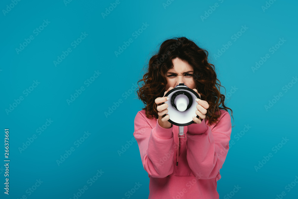 Fototapeta premium curly redhead girl covering face with megaphone while screaming on blue