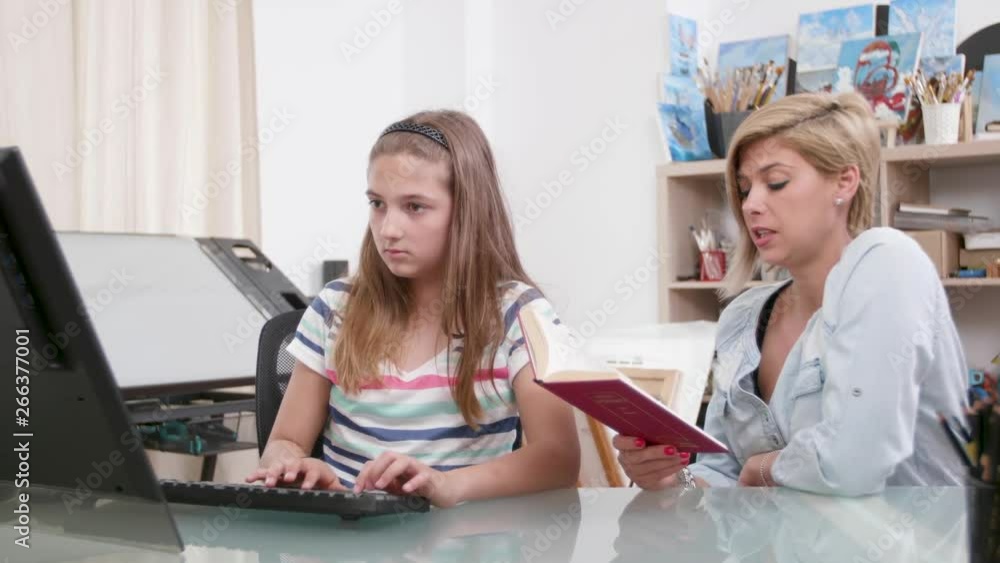 Mother helping her daughter to improve her typing skills. Reading a book to her daughter so she can learn to type faster. Mother helping her daughter to improve her typing skills. Reading a book to her daughter so she can learn to type faster.