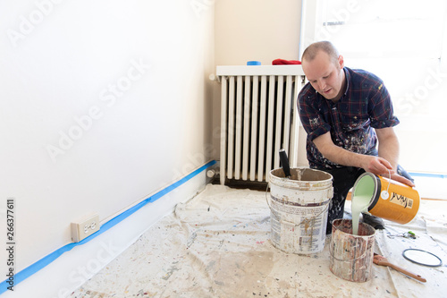 A young man pours house paint into a bucket. photo