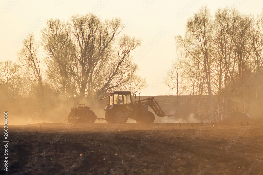 Fototapeta premium Sowing time. Blue tractor rides through the agricultural field in the sunlight.