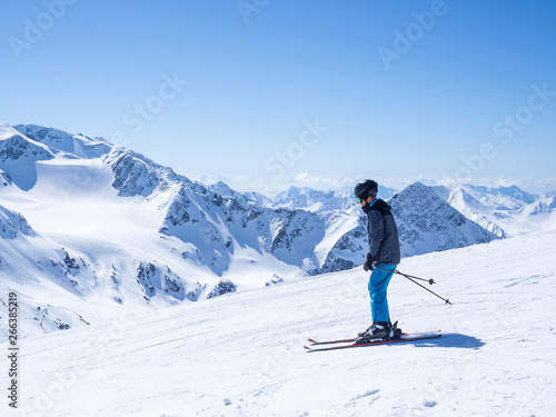 Skier at the top of Schaufelspitze mountain at Stubai Gletscher ski resort preparing to go down into the valley. Snow covered peaks. South Tyrol, Austrian Alps. Nature and sport background, blue sky