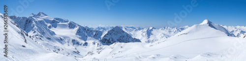 Panoramic landscape view from top of Schaufelspitze on winter landscape with snow covered mountain slopes and pistes at Stubai Gletscher ski resort at spring sunny day. Blue sky background. Stubaital