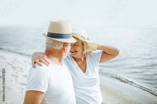 Happy senior couple dressed in white t-shirts and hats relaxing together on the sandy beach during their retirement