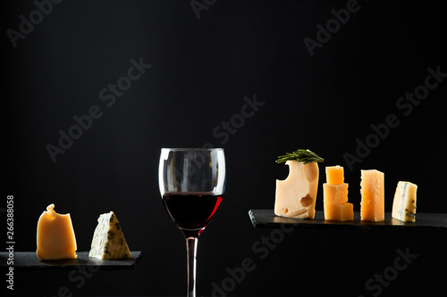 Fragrant red wine in glass beside sliced fresh cheese of different sorts