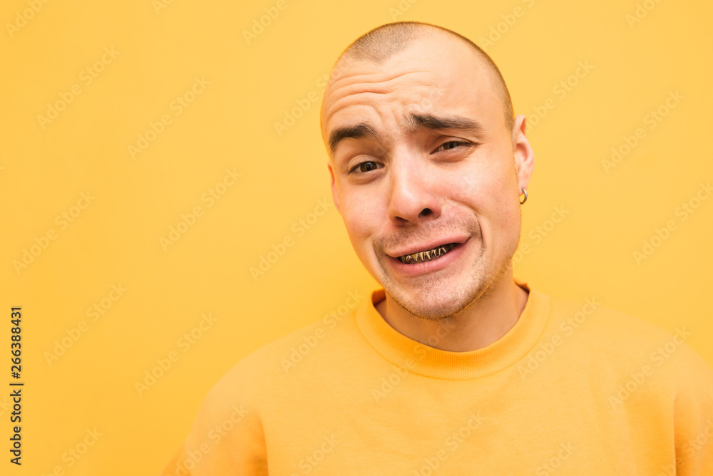 Obraz premium Сheerful guy in yellow clothes makes a funny face, a close-up portrait on a yellow background, wearing grillz teeth. Portrait of a fun rapper.