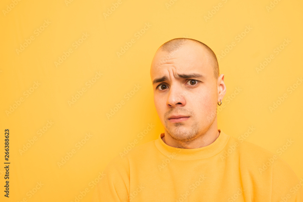 Close-up portrait of a frightened young man on a yellow background wearing yellow clothes and looking into the camera. Afraid guy with a funny face is isolated on a yellow background. Close-up portrait of a frightened young man on a yellow background wearing yellow clothes and looking into the camera. Afraid guy with a funny face is isolated on a yellow background.