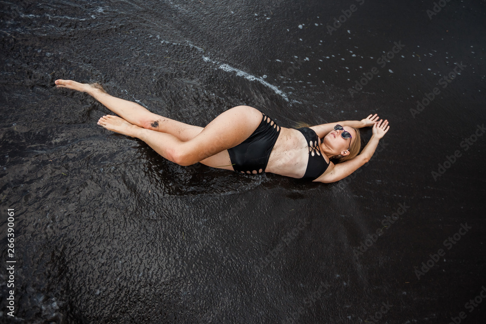 Fototapeta premium The girl in the swimsuit, lying on the black sand.