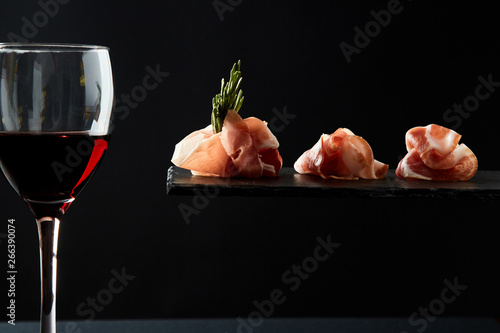 Composition of red wine in glass and pieces of meat snack on black background