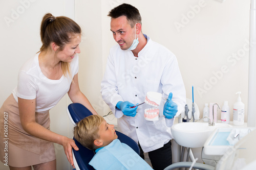 Stomatologist in uniform is telling to young boy and mother about hygiene