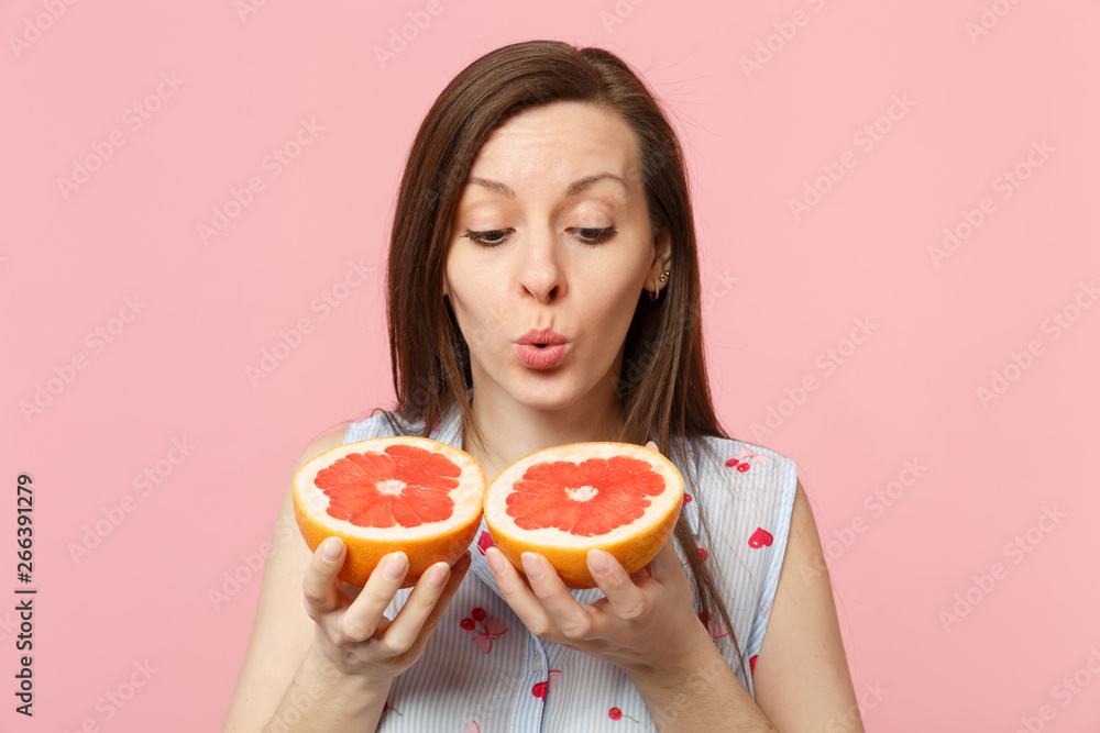 Pretty young woman in summer clothes holding in hands looking on halfs of fresh ripe grapefruit isolated on pink pastel background. People vivid lifestyle relax vacation concept. Mock up copy space. Pretty young woman in summer clothes holding in hands looking on halfs of fresh ripe grapefruit isolated on pink pastel background. People vivid lifestyle relax vacation concept. Mock up copy space.