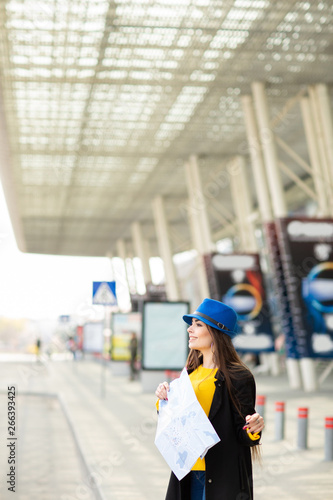 Beautiful young girl with a backpack behind her shoulder holding a map, in the street near the airport