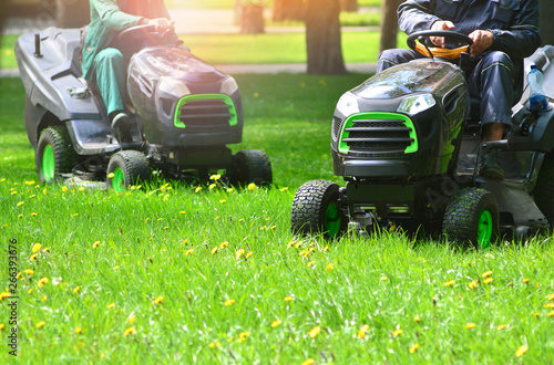 Fotografie Two lawn mowers trimming green grass on a meadow.