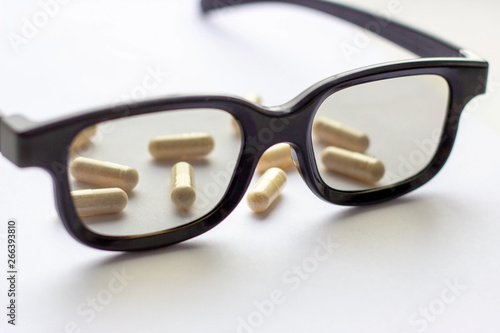 Pills, capsules and tablets with glasses on light background. Pharmacy and medicine concept. Focused on a pharmaceutical industry for eye diseases. Selective focus photography